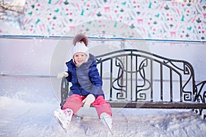 Little girl sitting on a bench in the skating rink