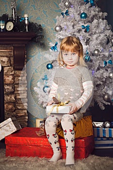 Little girl sitting on big present near the christmas tree