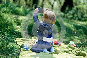 Little girl sitting on a blanket in a meadow and holds a phone. Back view