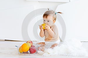 A little girl is sitting in a bright room with a plate of fruit and eating a pear