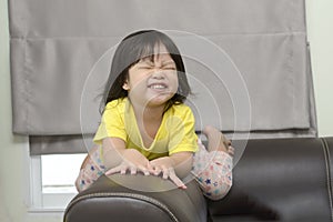 Little girl sitting on brown sofa making funny faces into the camera