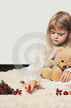 Little girl sitting on the carpet, with her teddy bear, playing with Christmas decoration