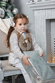 Little girl sitting in a chair with christmas box at hands.