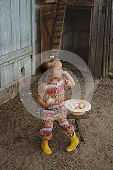 A little girl is sitting at the chicken coop and holding fresh eggs in her hands.