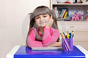 Little girl sitting in the children room at the table with color
