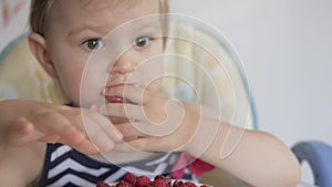 A little girl sitting at a children`s table eats ripe red raspberries