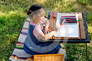 A little girl is sitting on the cloth and playing a toy befor painted on the paper