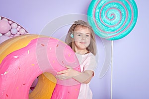 Little girl sitting in colorful room around big toyful candies, donut, lollipop