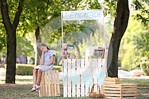 Little girl sitting on crate near lemonade stand in park