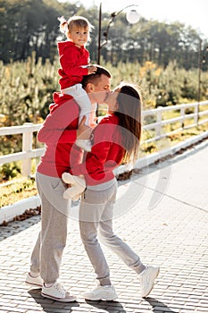 Little girl sitting on dad`s shoulders on nature. Mom, dad and daughter, walk in the autumn park. Happy young family spending tim