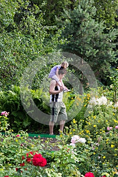 Little girl sitting on the daddy shoulders among flowers