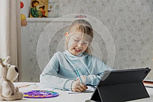 Little girl sitting at desk, doing homework using laptop in bedroom