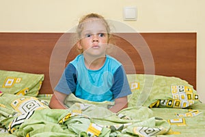 Little girl sitting on a double bed and frightened looks into distance
