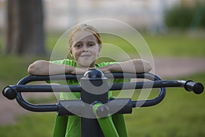 Little girl sitting on exercise equipment in the public park.