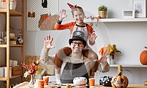 Little girl sitting on father shoulders making scary gesture while making Halloween home decorations