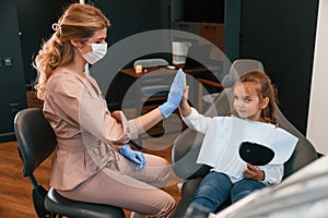Little girl is sitting with the female doctor. In the stomatological cabinet