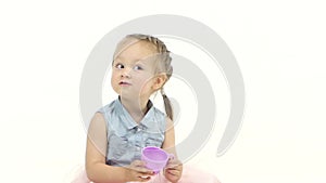 Little girl is sitting on the floor holding a cup. White background. Slow motion