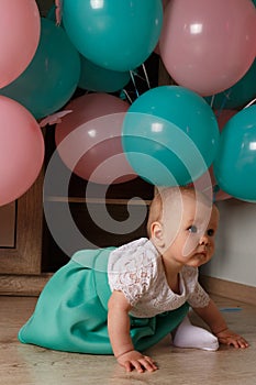 Little girl sitting on the floor in the room next to the balloons, first birthday, celebrate. one year old blue and pink balls wit