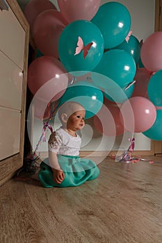 Little girl sitting on the floor in the room next to the balloons, first birthday, celebrate. one year old blue and pink balls wit