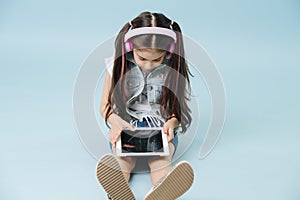 Little girl sitting on the floor, watching tablet with wireless headphones