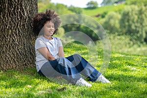 Little girl sitting on grass under tree resting in nature enjoying freshair.