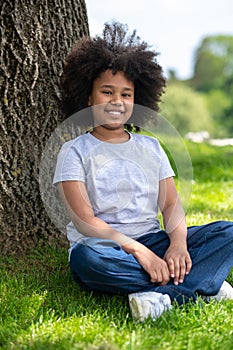 Little girl sitting on grass under tree resting in nature enjoying freshair.