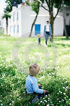 Little girl sitting on green grass and looking at people walking by