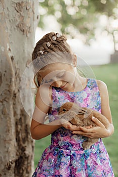 Little girl sitting on the green grass with rabbit. Cute child girl holding a bunny in her hands on Easter day