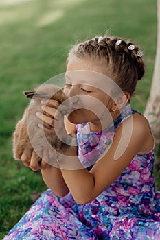 Little girl sitting on the green grass with rabbit. Cute child girl holding a bunny in her hands on Easter day