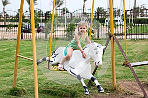 Little girl sitting on harseback of children swing, swinging on playground