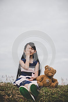 Little girl sitting with her bear upset at meadows field.