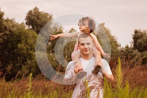 Little girl is sitting on her father`s shoulders in the summer in the park