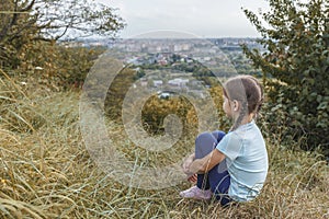 Little girl sitting on a hill above the city.