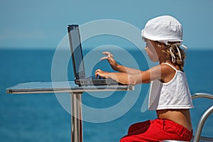 Little girl sitting at laptop at background of sea