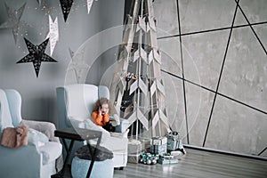 Little girl sitting in the living room near a stylized Christmas tree.