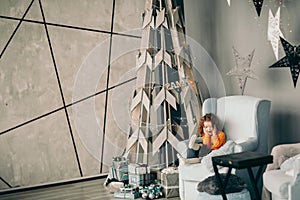 little girl sitting in the living room near a stylized Christmas tree.
