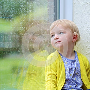 Little girl sitting next window on rainy day