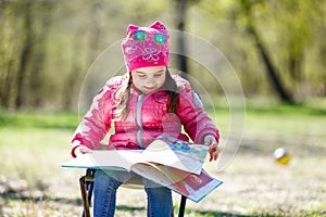 Little girl sitting in over-sized rocking chair pretending to read to her teddy bear