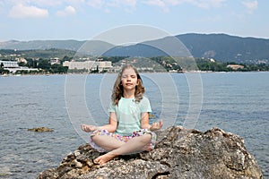 Little girl sitting on a rock and meditates