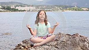 Little girl sitting on a rock and meditates