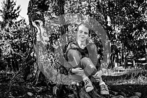 Little girl sitting on the roots of a birch. Black and white photo.