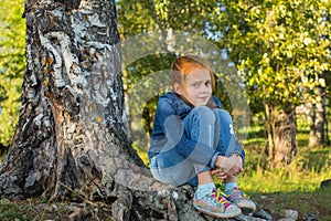 Little girl sitting on the roots of a birch. Nature.