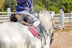 Little girl sitting in a saddle on a horse back and having fun riding along wooden fence at farm or ranch