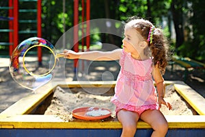 Little girl sitting in a sandbox and blows the big