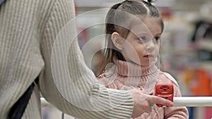 Little girl is sitting in a shopping cart in a supermarket.