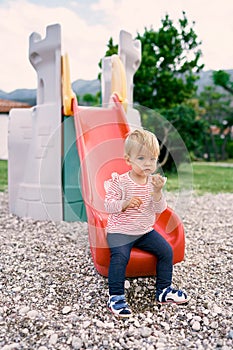 Little girl sitting on a slide in the park
