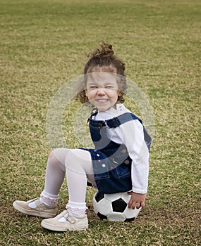 Little girl sitting on a soccer ball.