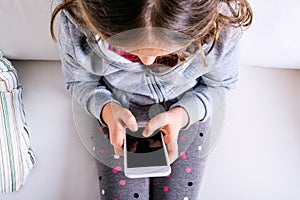Little girl sitting on sofa, playing with smartphone