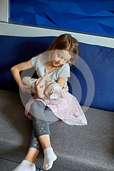 Little girl sitting on the sofa in the room at home playing with baby doll