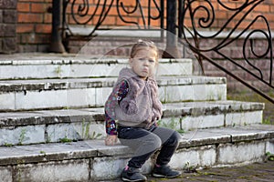Little girl sitting on stairs with lowered corners of the lips on her face